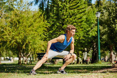 Buy stock photo Full length shot of a handsome and athletic young sportsman warming up before beginning his jog in the park