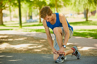 Buy stock photo Full length shot of a handsome and athletic young sportsman tying his laces during a jog in the park