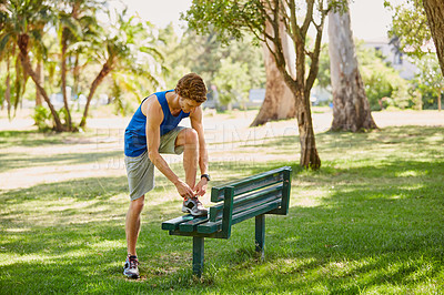 Buy stock photo Full length shot of a handsome and athletic young sportsman tying his laces during a jog in the park