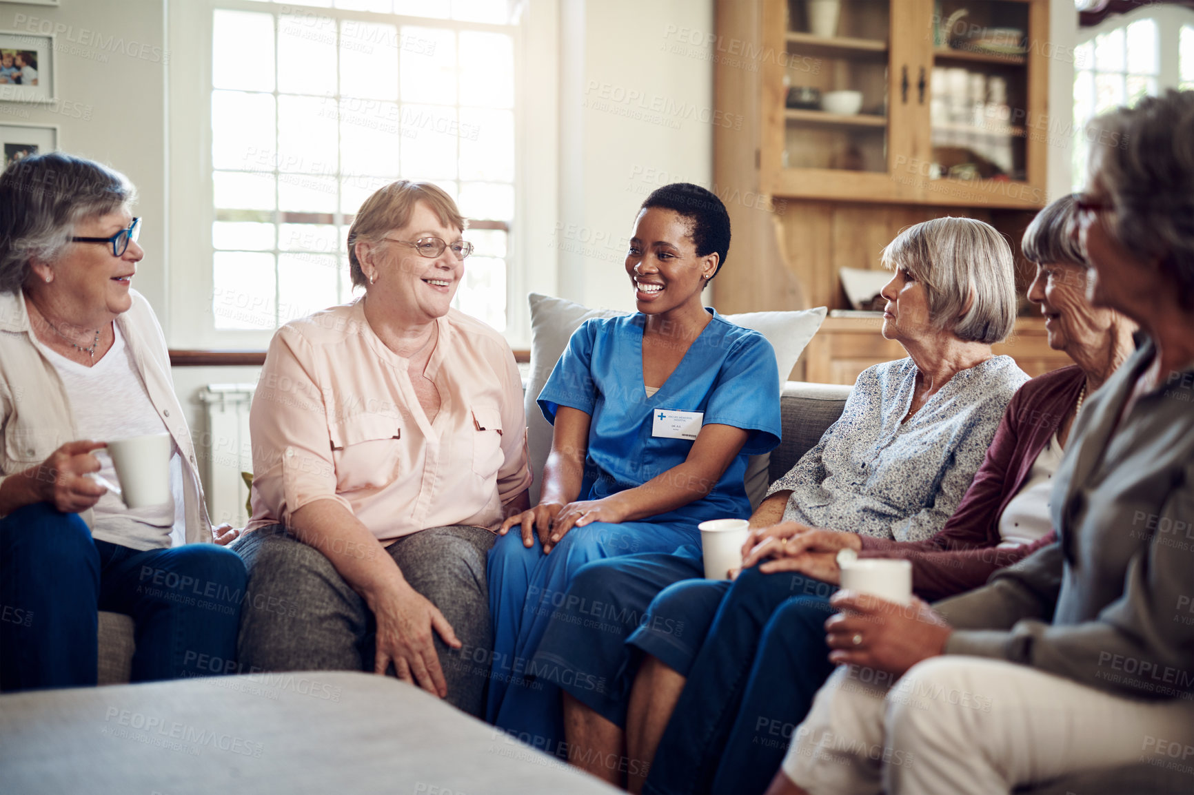 Buy stock photo Cropped shot of an attractive young nurse sitting with her senior patients in the living room of a nursing home