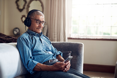 Buy stock photo Shot of a senior man using a smartphone and headphones while relaxing at home