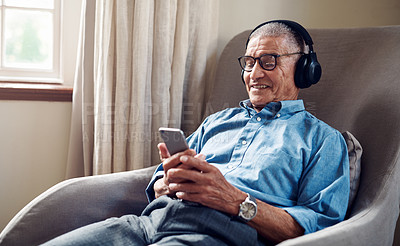 Buy stock photo Shot of a senior man using a smartphone and headphones while relaxing at home