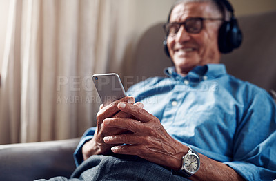 Buy stock photo Shot of a senior man using a smartphone and headphones while relaxing at home