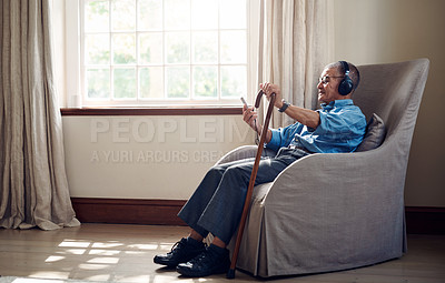 Buy stock photo Shot of a senior man using a smartphone and headphones while relaxing at home