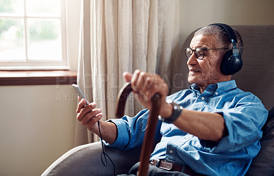 Buy stock photo Shot of a senior man using a smartphone and headphones while relaxing at home