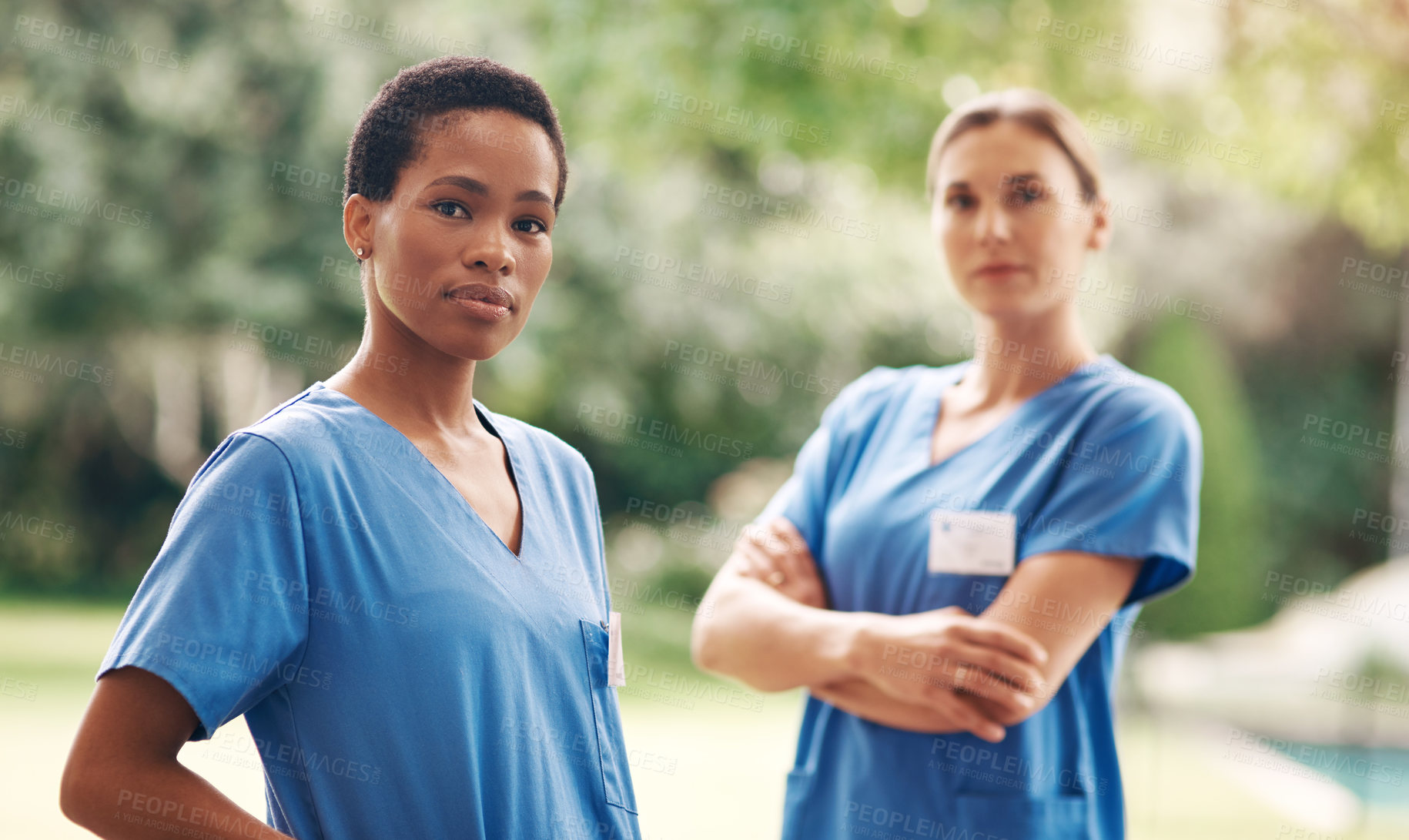 Buy stock photo Portrait of two confident young nurses standing outside in the garden of a retirement home