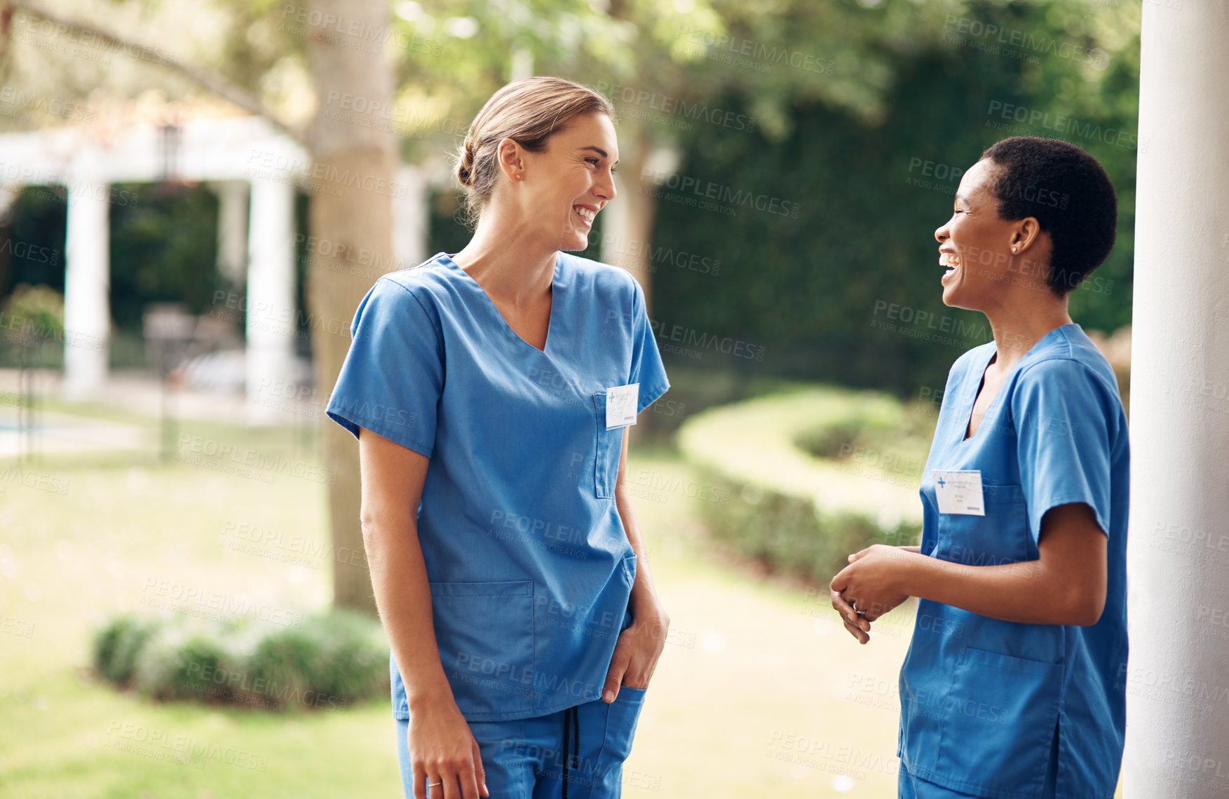 Buy stock photo Shot of two young nurses talking outside in the garden of a retirement home
