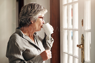 Buy stock photo Shot of a senior woman having coffee and looking thoughtfully out of a window