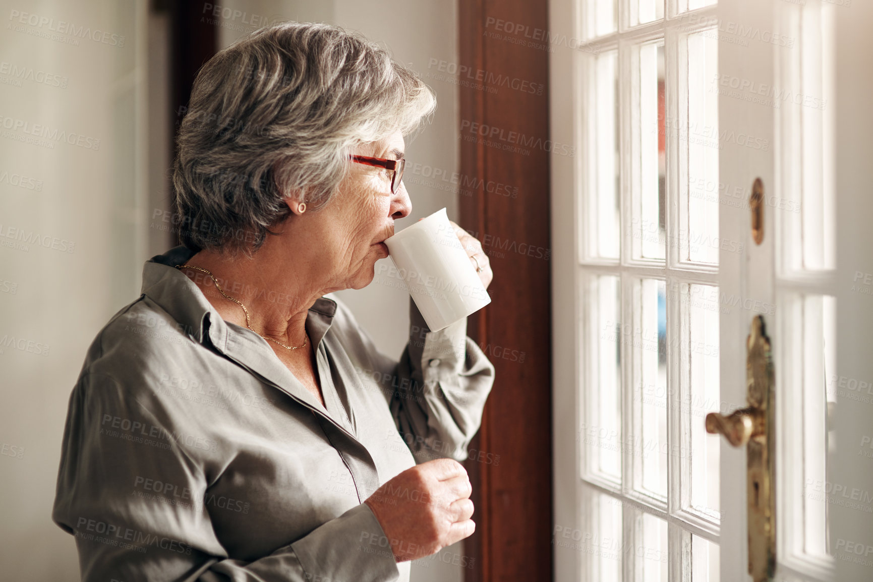 Buy stock photo Shot of a senior woman having coffee and looking thoughtfully out of a window