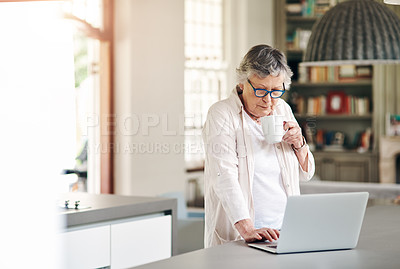 Buy stock photo Shot of a senior woman having coffee while using a laptop at home