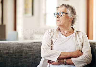 Buy stock photo Shot of a senior woman sitting on the sofa at home and looking thoughtful