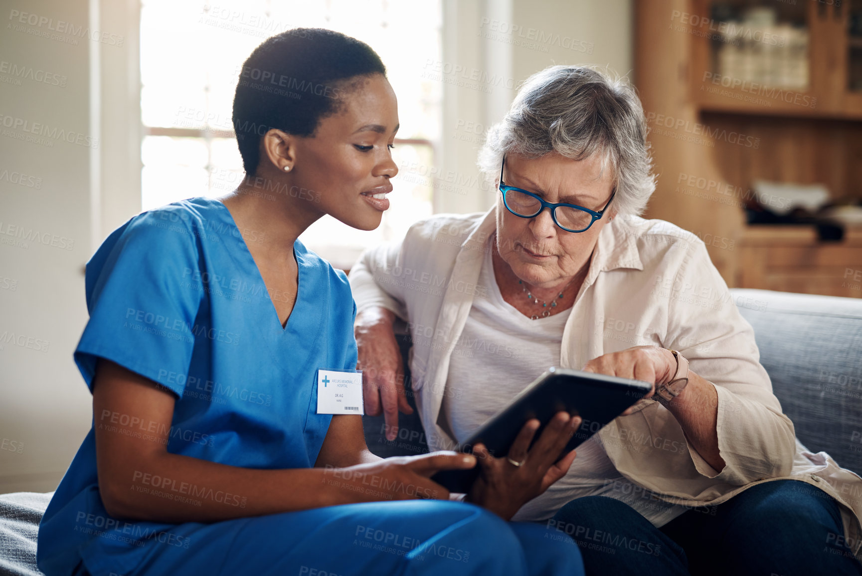 Buy stock photo Shot of a senior woman using a digital tablet with a nurse on the sofa at home