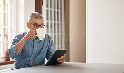 Buy stock photo Shot of a senior man having coffee and using a digital tablet at home