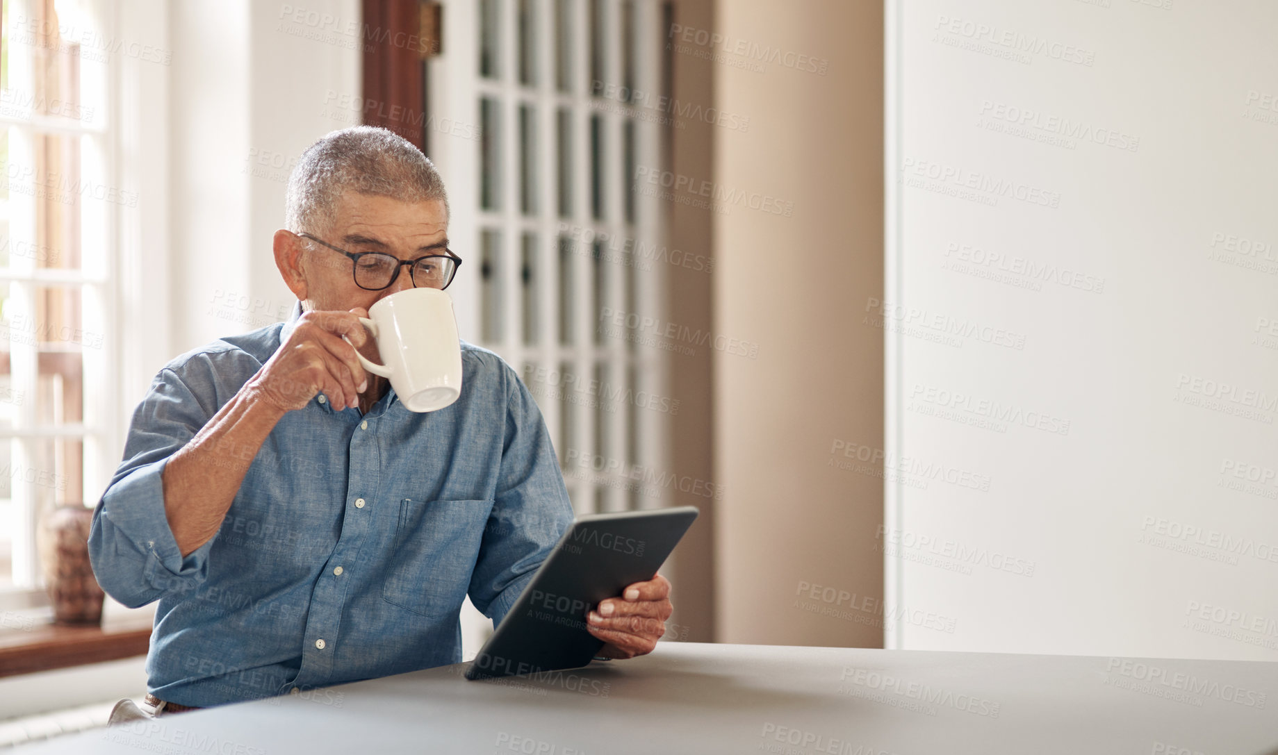 Buy stock photo Shot of a senior man having coffee and using a digital tablet at home