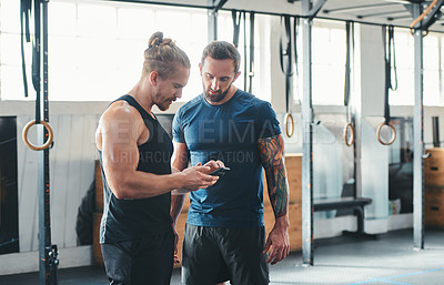 Buy stock photo Cropped shot of two handsome young male athletes looking at a cellphone while standing in the gym