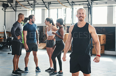 Buy stock photo Cropped portrait of a handsome young male athlete standing in the gym with other gym-goers in the background