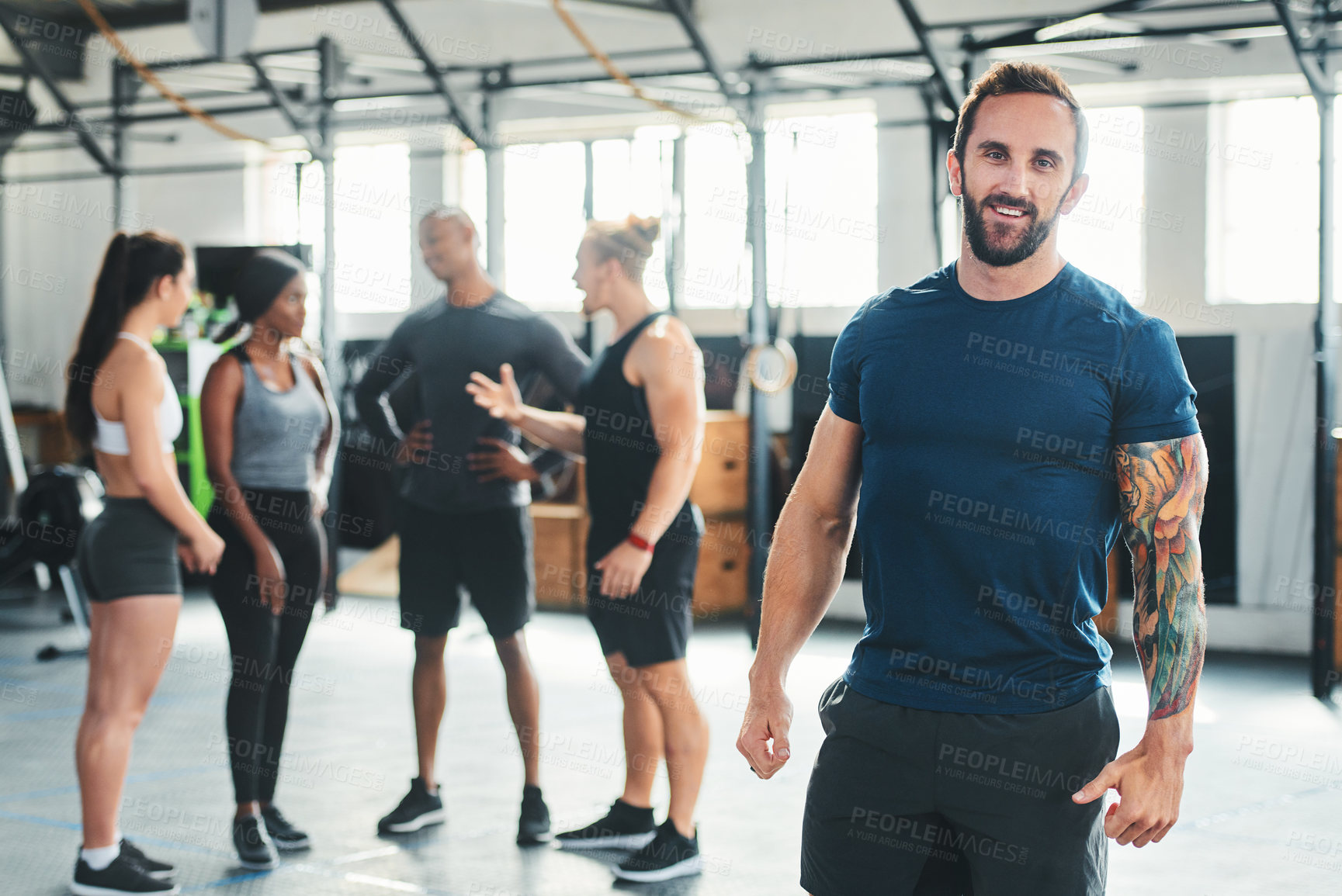 Buy stock photo Cropped portrait of a handsome young male athlete standing in the gym with other gym-goers in the background