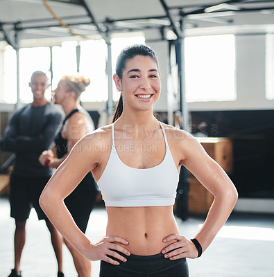 Buy stock photo Cropped portrait of an attractive young female athlete standing with her hands on her hips in the gym with other gym-goers in the background