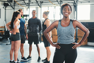 Buy stock photo Cropped portrait of an attractive young female athlete standing with her hands on her hips in the gym with other gym-goers in the background