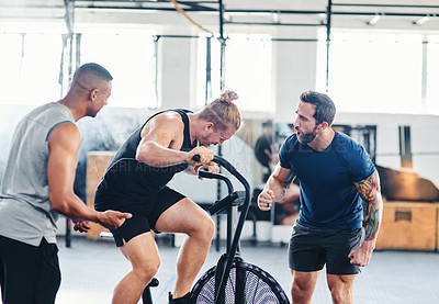 Buy stock photo Shot of a young male athlete working out on an exercise bike while his friends spur him on