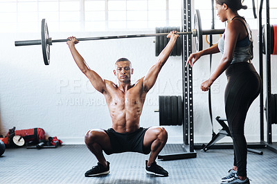 Buy stock photo Shot of a man working out with the help of his coach at the gym