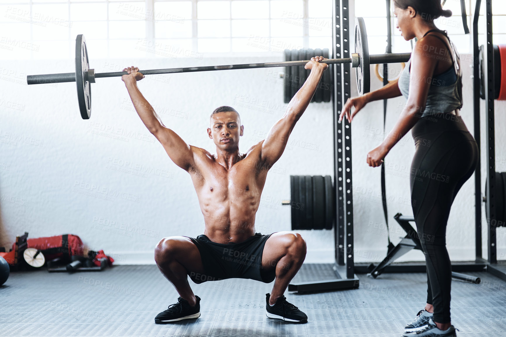 Buy stock photo Shot of a man working out with the help of his coach at the gym