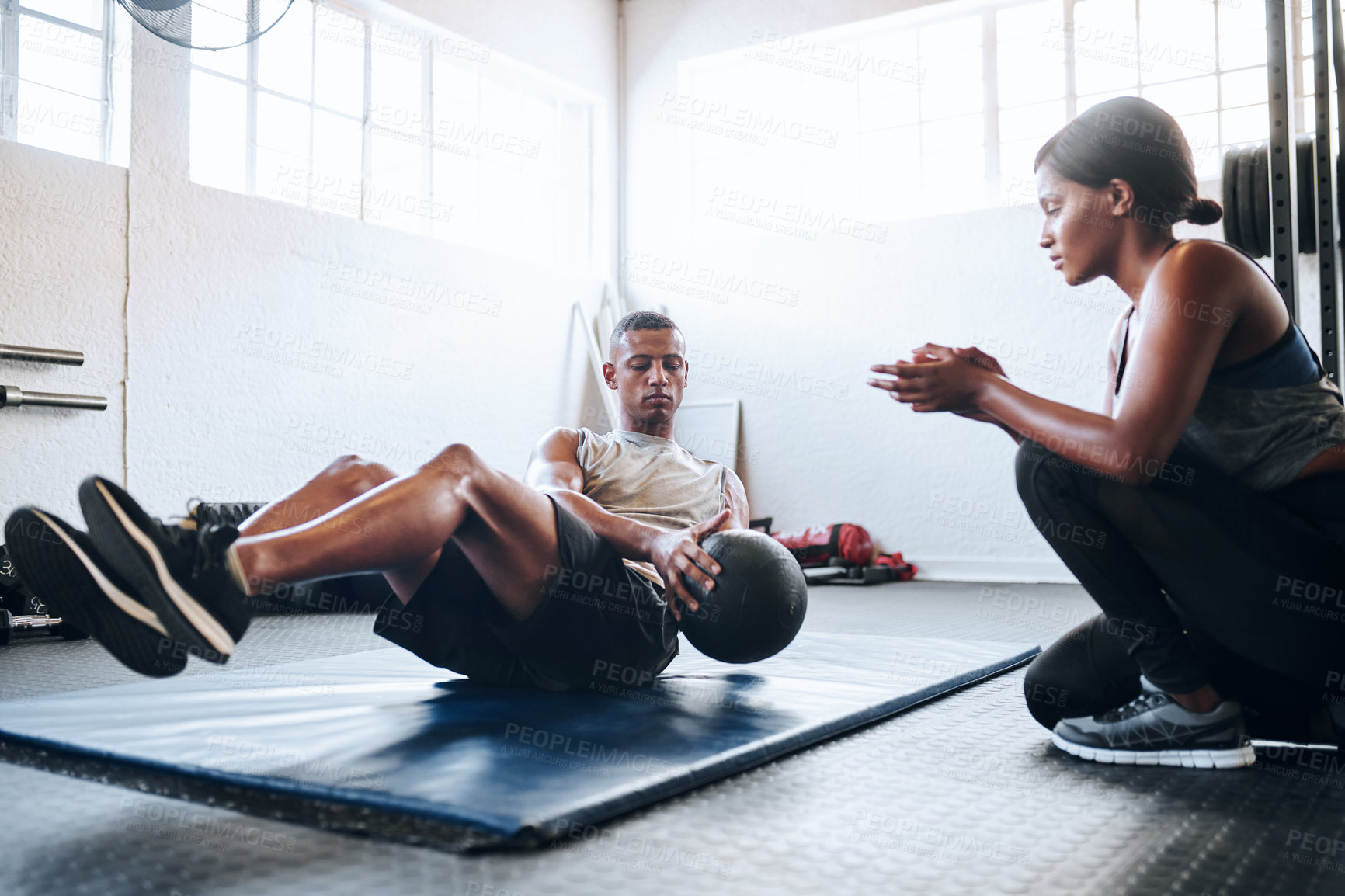 Buy stock photo Shot of a man working out with the help of his coach at the gym
