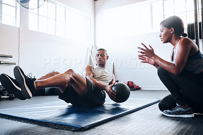 Buy stock photo Shot of a man working out with the help of his coach at the gym