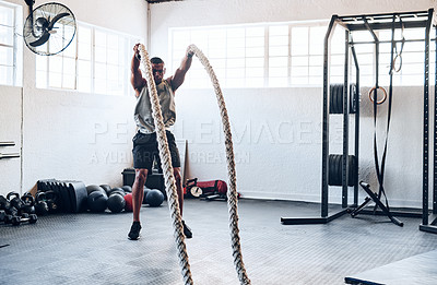 Buy stock photo Shot of a muscular young man working out with battle ropes at the gym