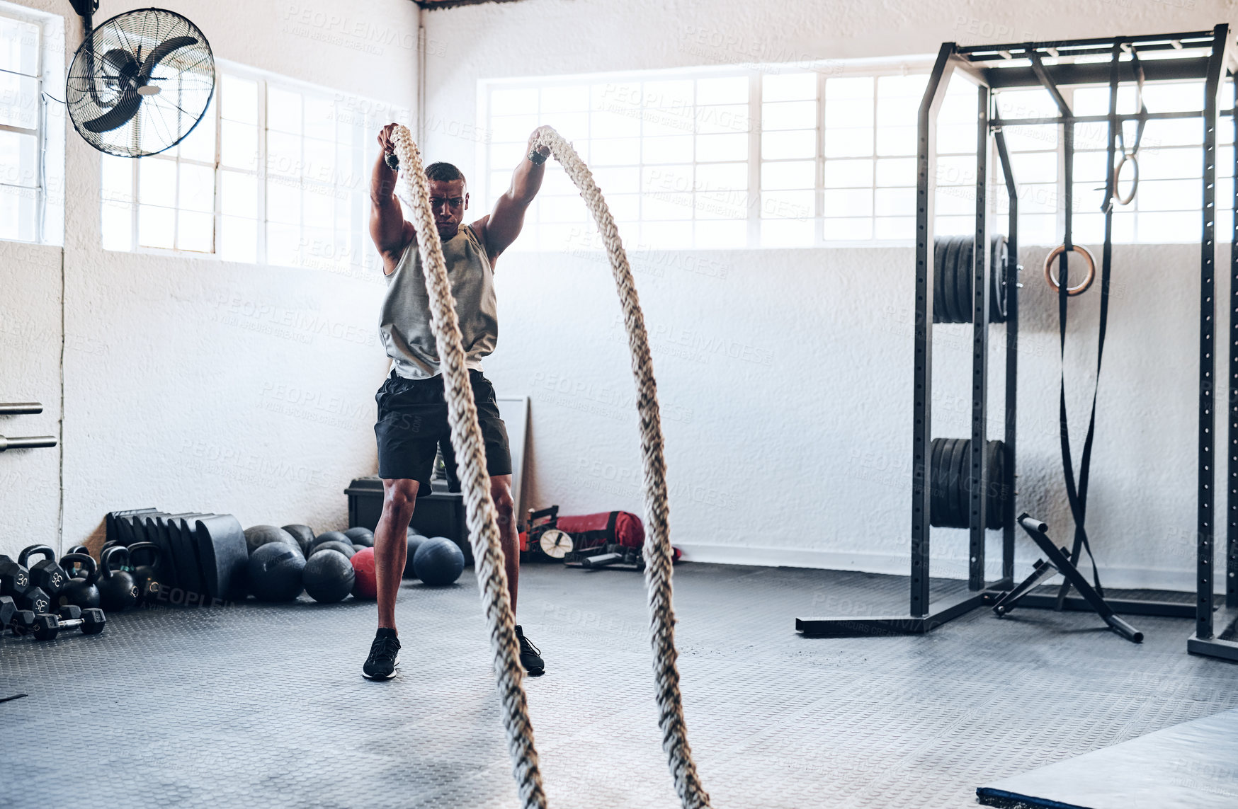 Buy stock photo Shot of a muscular young man working out with battle ropes at the gym