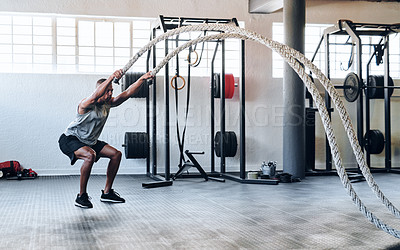 Buy stock photo Shot of a muscular young man working out with battle ropes at the gym