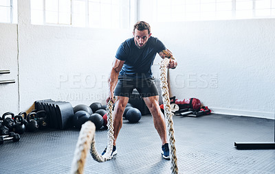Buy stock photo Shot of a muscular young man working out with battle ropes at the gym