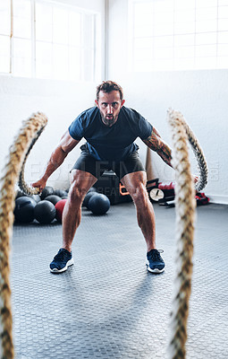 Buy stock photo Shot of a muscular young man working out with battle ropes at the gym