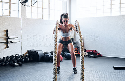 Buy stock photo Shot of a fit young woman working out with battle ropes at the gym