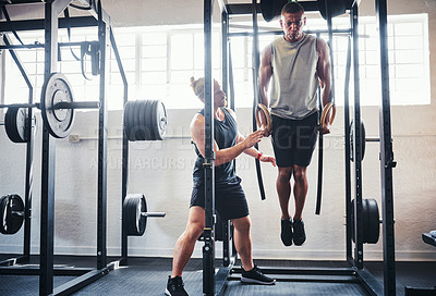 Buy stock photo Shot of a man working out with the help of his coach at the gym