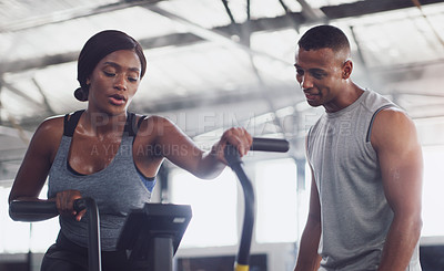 Buy stock photo Shot of a young woman working out on an exercise bike with her trainer in a gym