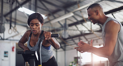 Buy stock photo Shot of a young woman working out on an exercise bike with her trainer in a gym