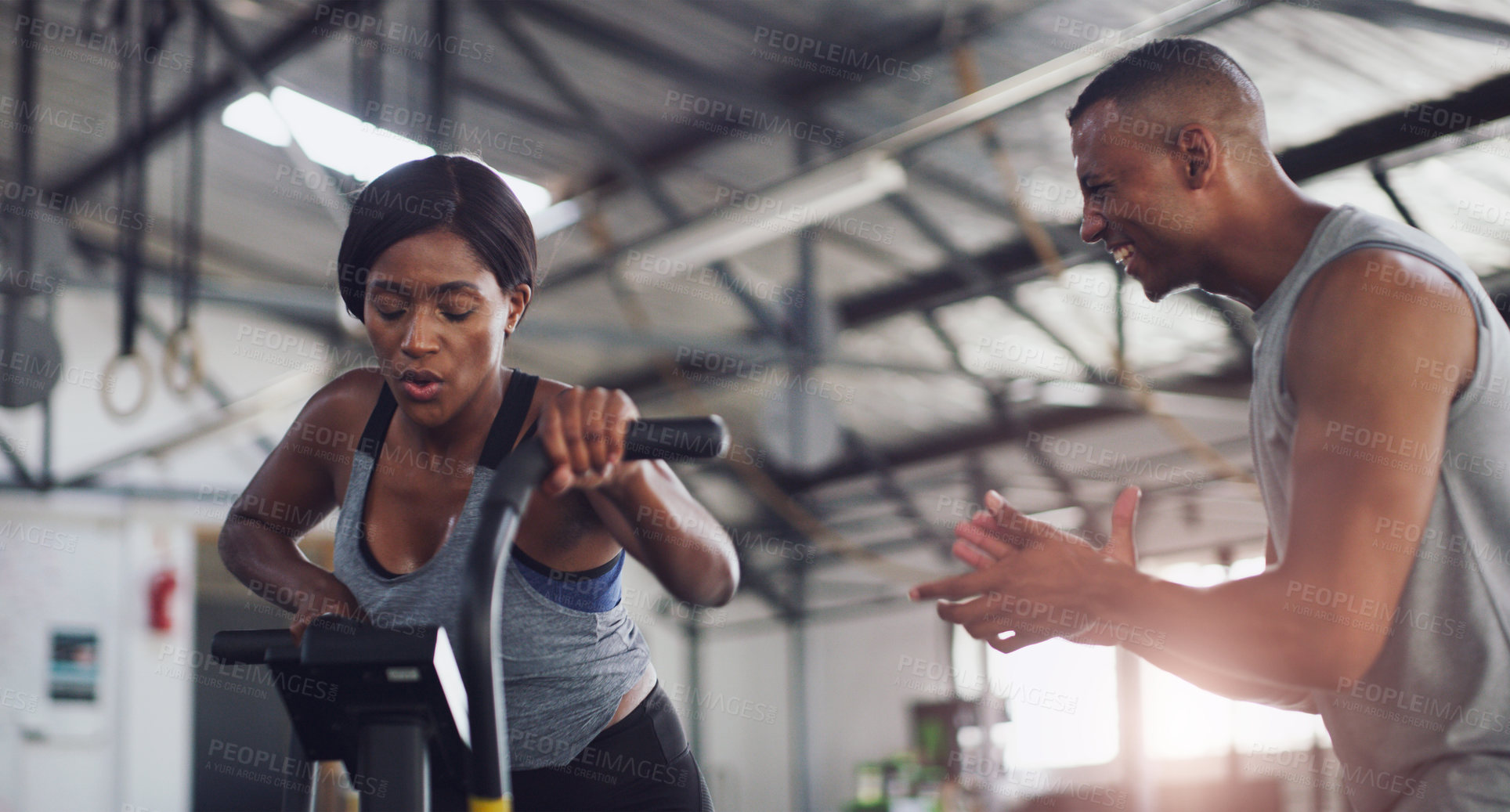 Buy stock photo Shot of a young woman working out on an exercise bike with her trainer in a gym