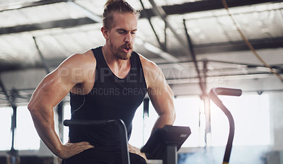 Buy stock photo Shot of a young man taking a break while working out on an exercise bike in a gym