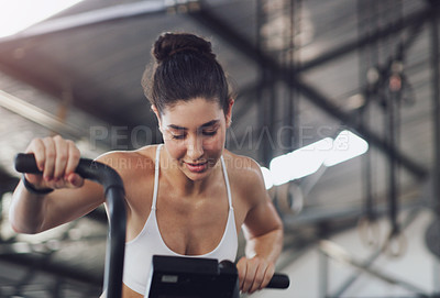 Buy stock photo Shot of a young woman working out on an exercise bike in a gym