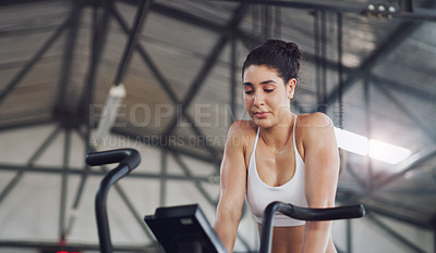 Buy stock photo Shot of a young woman working out on an exercise bike in a gym