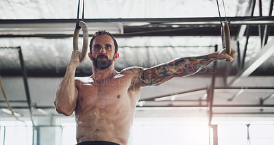 Buy stock photo Shot of a young man exercising with gymnastic rings in a gym