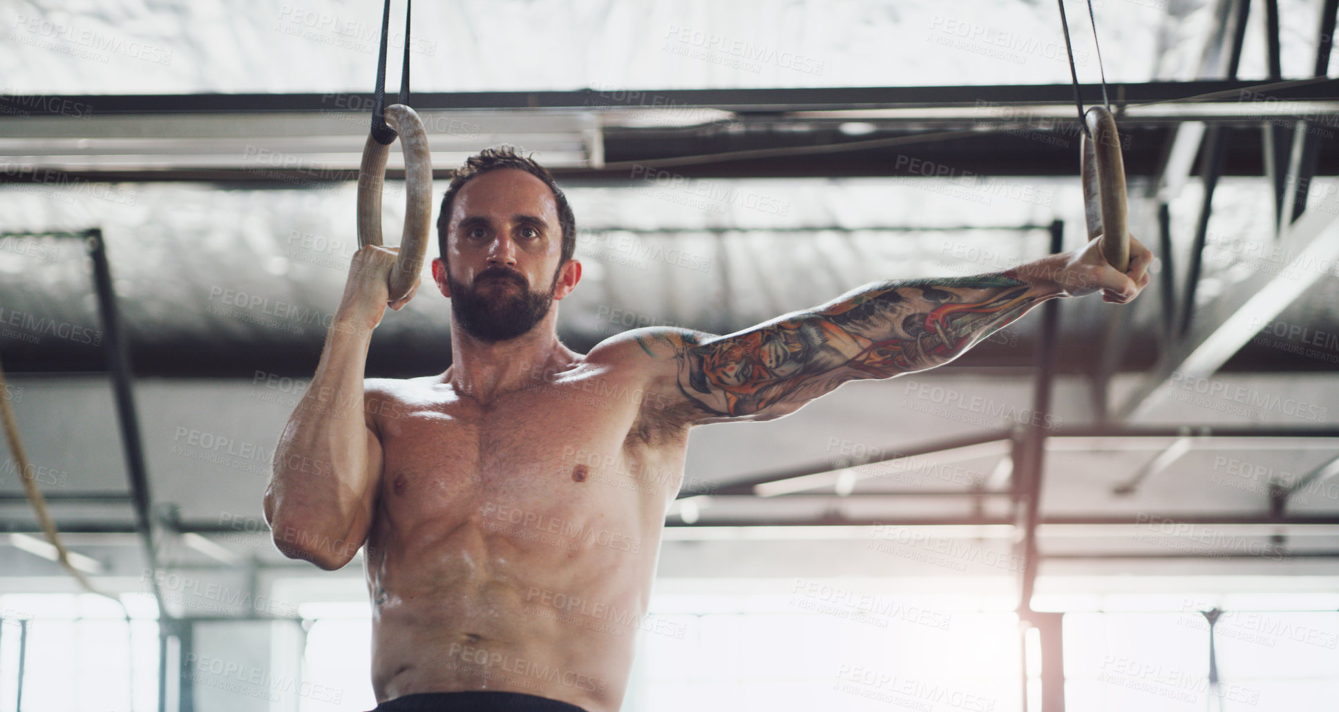 Buy stock photo Shot of a young man exercising with gymnastic rings in a gym