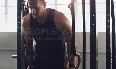 Buy stock photo Shot of a young man exercising with gymnastic rings in a gym