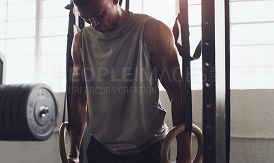 Buy stock photo Shot of a young man exercising with gymnastic rings in a gym