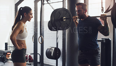 Buy stock photo Shot of a man exercising with a barbell with the help of a trainer in a gym