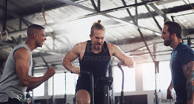 Buy stock photo Shot of a young man working out on an exercise bike while his friends encourage him in a gym