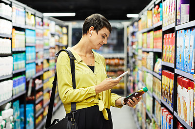 Buy stock photo Shot of a young woman using her phone while browsing in a supermarket