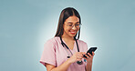 Happy, woman and nurse with phone in studio with telehealth, communication or texting on mobile app. Smile, tech and pediatric healthcare worker with cellphone for medical research on blue background