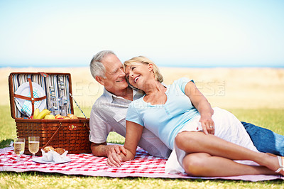 Buy stock photo An affectionate mature couple enjoying a picnic at the coast on a sunny day